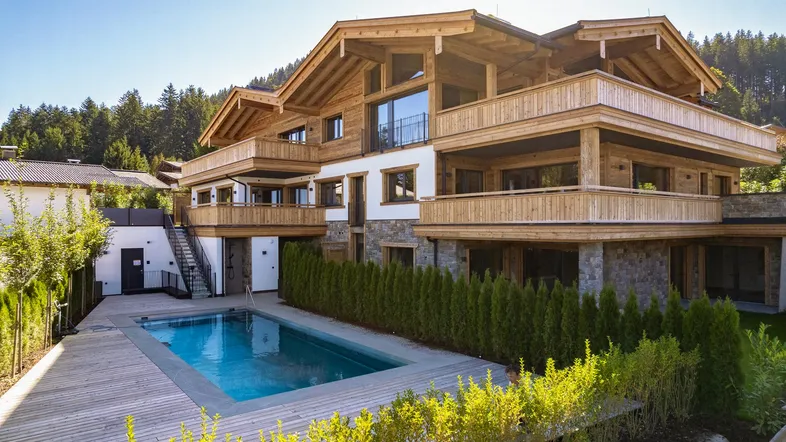 Luxuriöses Chalet mit Außenpool und Holzfassade, umgeben von grüner Natur und Bergen.