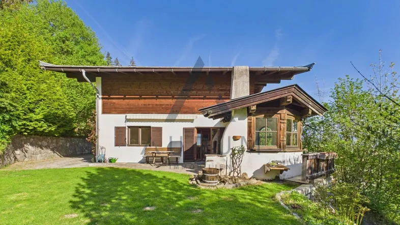 Traditionelles Haus mit Holzfassade, Garten und Sitzbereich im Freien unter blauem Himmel.