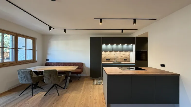 Moderne offene Küche mit dunklen Schränken, Holzarbeitsplatten und Essbereich mit Holztisch und Bank.