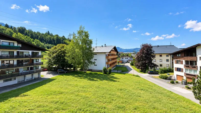Weitläufige Grünfläche umgeben von Wohngebäuden mit Bergblick unter blauem Himmel.