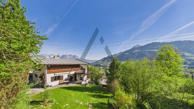 Großzügiger Gartenbereich mit Rasenfläche und einem charmanten Haus im alpinen Stil, umgeben von Bergen.