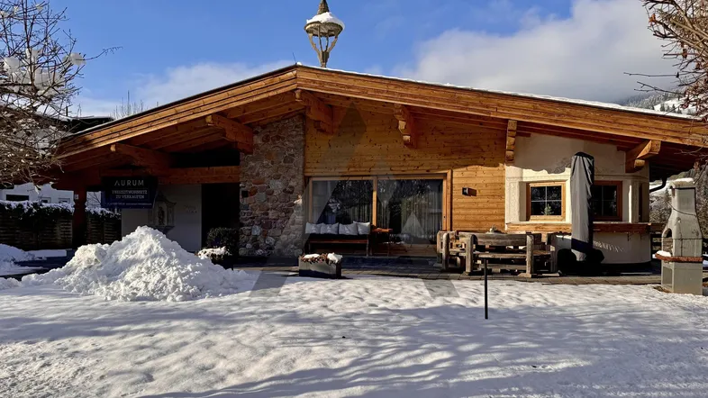 Traditionelles Holzhaus im alpinen Stil mit Steinelementen und verschneiter Terrasse im Winter.