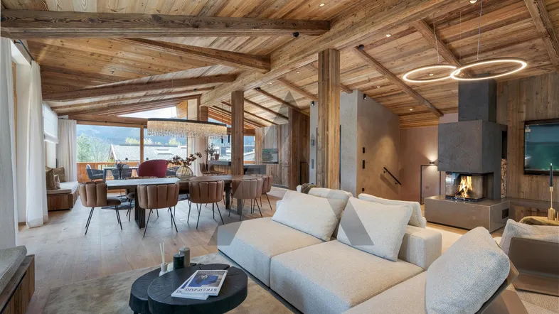 Geräumiger Wohn-Essbereich im Chalet-Stil mit Holzbalkendecke, Kamin und Zugang zum Balkon mit Bergblick.