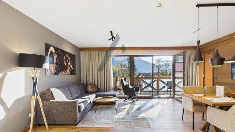 Geräumiger Wohn-Essbereich mit Holzboden, bequemer Couch und Zugang zum Balkon mit Bergblick.