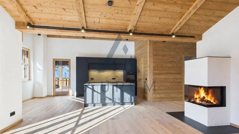 Geräumiger offener Wohnbereich mit Holzbalkendecke, Kamin und moderner Einbauküche mit Insel.