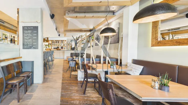 Gemütlicher Restaurantbereich mit Holztischen, Sitzbänken und einer Bar im Hintergrund, geprägt von rustikalen Holzelementen.