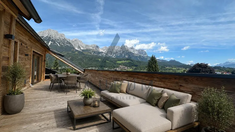 Geräumige Holzterrasse mit modernen Loungemöbeln und Esstisch, bietet einen spektakulären Bergblick.