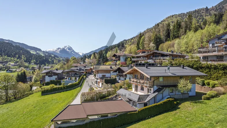 Panoramablick auf ein charmantes Bergdorf mit traditionellen Häusern und schneebedeckten Gipfeln im Hintergrund.