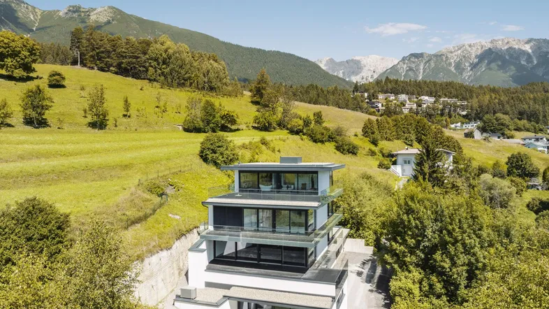 Moderne Villa mit mehreren Terrassen und Bergblick in grüner Umgebung.
