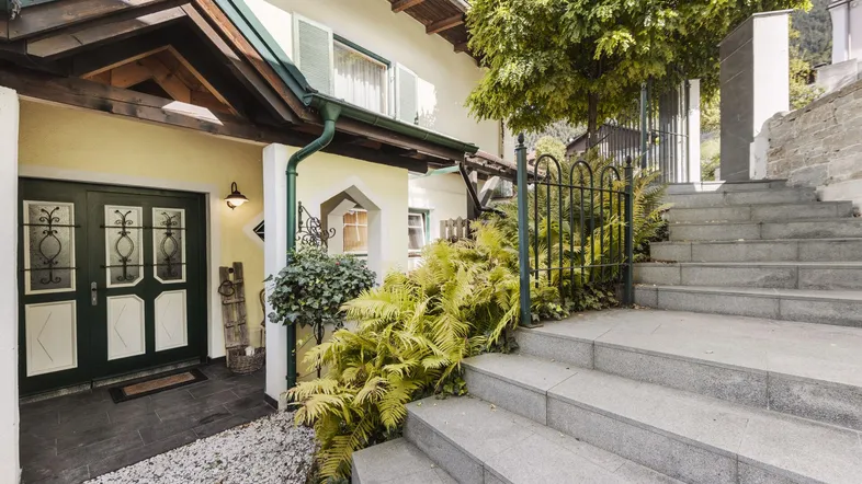 Traditionelles Haus mit Steintreppe und grüner Bepflanzung am Eingangsbereich.