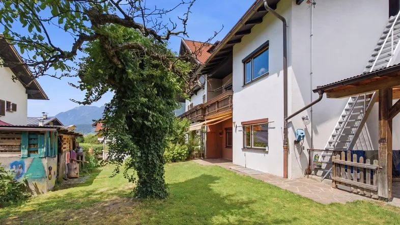 Seitlicher Blick auf das Haus mit gepflegtem Rasen, altem Baum und Zugang zum Gartenbereich.