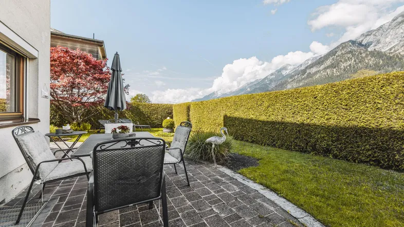 Gemütliche Terrasse mit Gartenmöbeln, umgeben von einer Hecke und mit Bergblick.