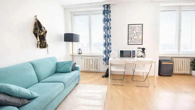 Helles Wohnzimmer mit türkisfarbenem Sofa, Holzboden und einem kleinen Essbereich am Fenster.