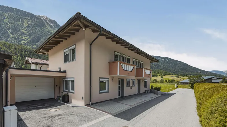 Ansicht des Mehrfamilienhauses mit Garage und Balkonen vor alpiner Bergkulisse.