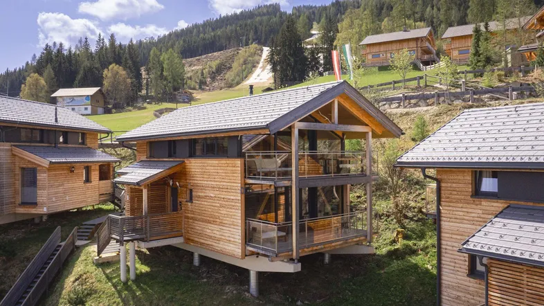 Modernes Holzchalet mit großen Glasfronten und Balkonen in alpiner Hanglage.