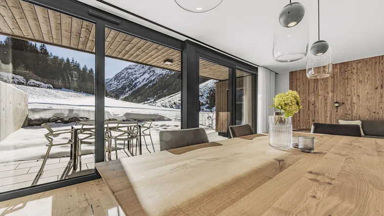 Heller Essbereich mit großem Holztisch, modernen Pendelleuchten und Zugang zur verschneiten Terrasse mit Bergblick.