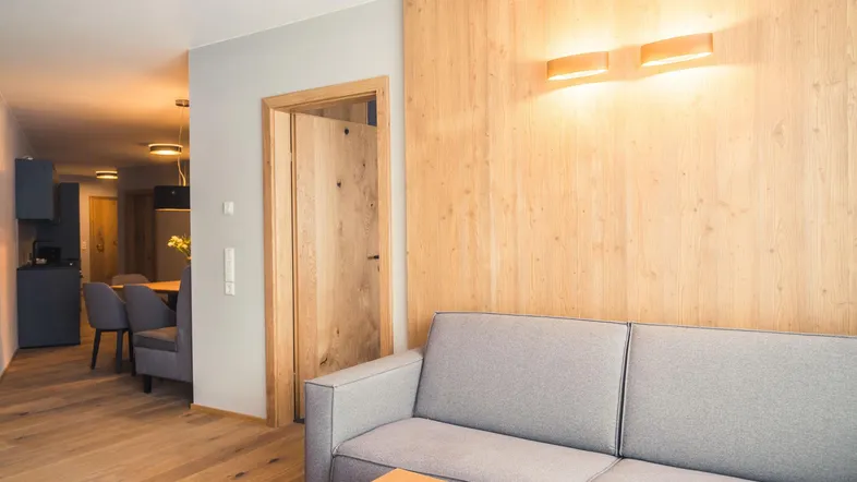Modernes Wohnzimmer mit Holzwandverkleidung, bequemer Couch und Blick in den Essbereich.