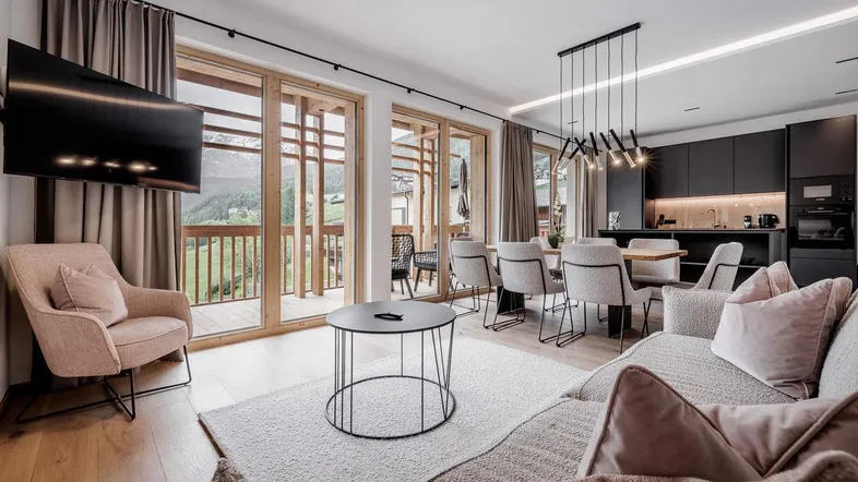 Moderner offener Wohn-Essbereich mit integrierter Küche, Holzboden und Zugang zum Balkon mit Bergblick.
