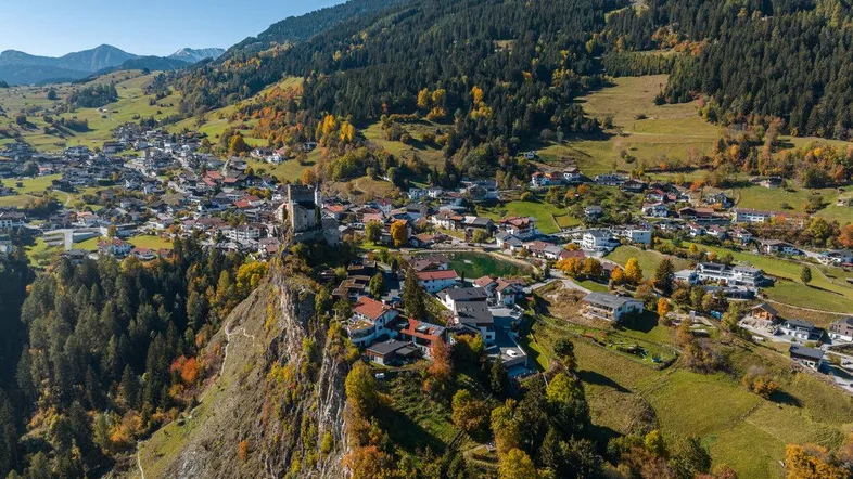 Luftaufnahme eines malerischen Bergdorfes in den Alpen mit umliegenden Wäldern und Bergen.