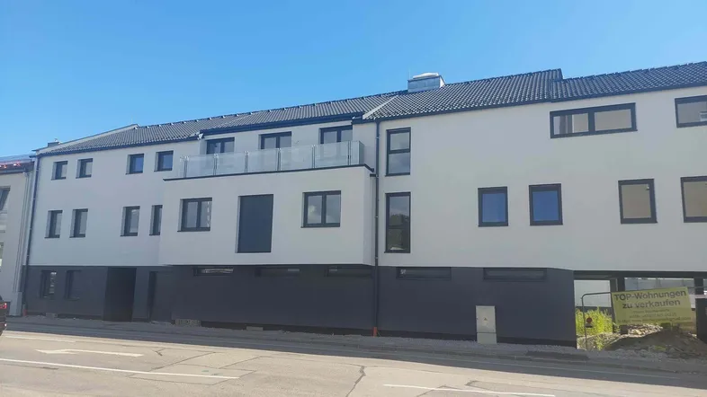 Modernes Mehrfamilienhaus mit weißer Fassade, dunklem Dach und Balkonen, ideal für neue Wohnungen.