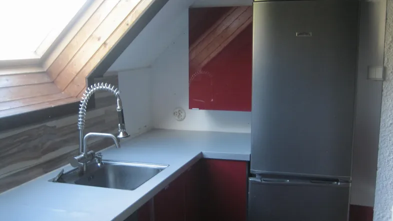 Dachgeschossküche mit roter Front, Spüle und Kühlschrank unter einem Dachfenster.