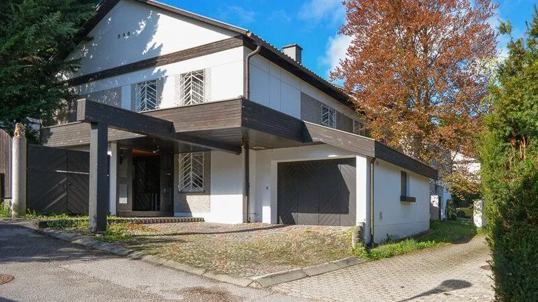 Einfamilienhaus mit Carport und Garage, umgeben von Bäumen unter blauem Himmel.