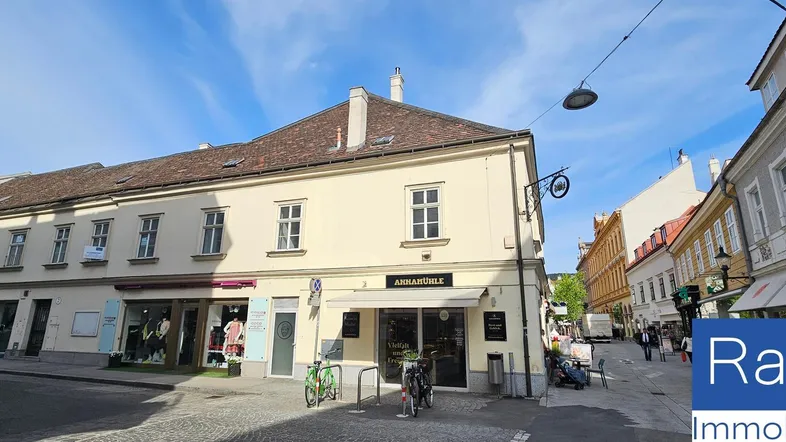 Historisches Gebäude mit Geschäften im Erdgeschoss an einer belebten Straße in der Stadt.