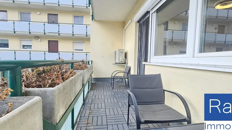 Heller Balkon mit Fliesenboden, Sitzgelegenheiten und Blick auf die umliegenden Gebäude.