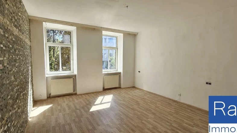 Heller Wohnraum mit Laminatboden, einer Steinwand und zwei großen Fenstern, die viel Tageslicht hereinlassen.