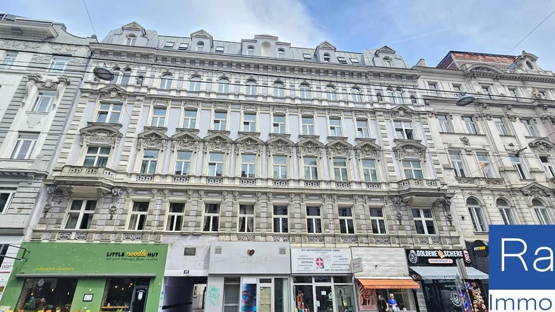 Historisches Gebäude mit reich verzierter Fassade und Geschäften im Erdgeschoss in einer Stadtansicht.