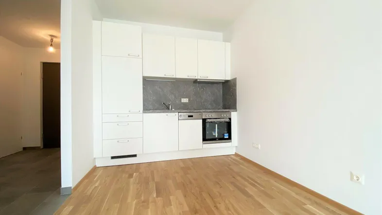 Moderne Einbauküche in Weiß mit integrierten Geräten und hellem Parkettboden in einem offenen Wohnbereich.