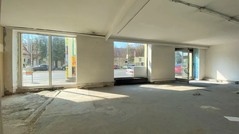 Geräumiger, leerstehender Gewerberaum mit großen Schaufenstern zur Straße und Betonboden, ideal für Umbau.