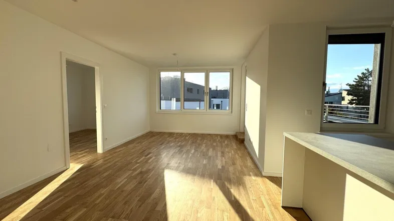 Helles Wohnzimmer mit Parkettboden, großen Fenstern und viel Tageslicht, angrenzend an einen Küchenbereich.
