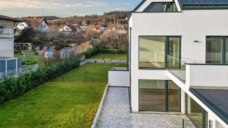 Moderne Doppelhaushälfte mit großem Garten, gepflasterter Terrasse und Blick auf die umliegende Wohngegend.