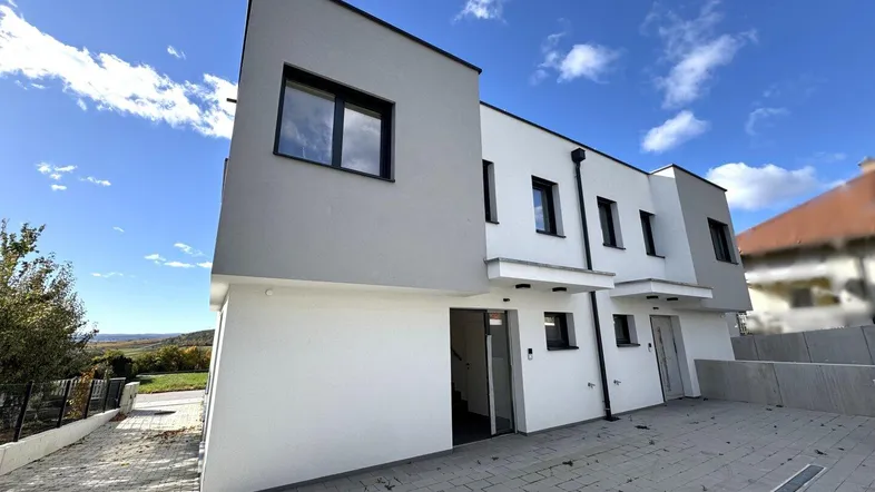 Moderne Reihenhäuser mit weißer und grauer Fassade unter blauem Himmel.