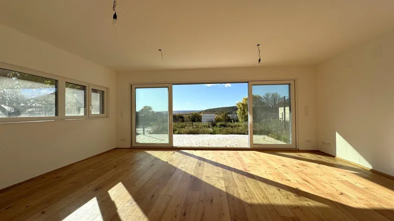 Helles Wohnzimmer mit Holzboden und großen Schiebetüren, die einen weiten Blick ins Grüne bieten.