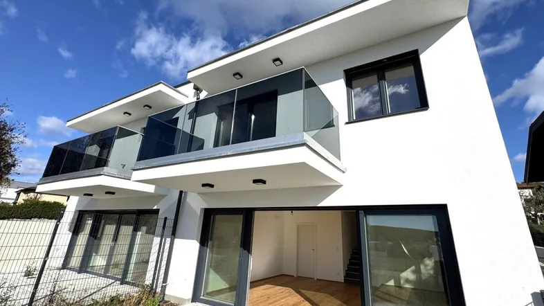 Moderne Reihenhäuser mit weißer Fassade, großen Fenstern und Balkonen mit Glasgeländer.