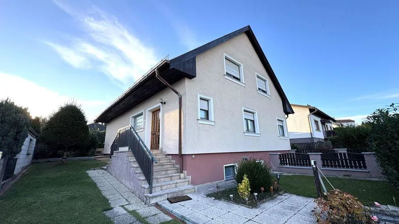 Vorderansicht des Hauses mit gepflegtem Vorgarten und Zugang über eine Außentreppe.