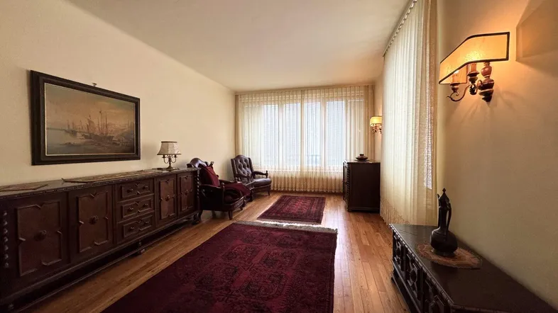 Geräumiges Wohnzimmer mit Holzboden, traditionellen Möbeln und großen Fenstern, die viel Licht hereinlassen.