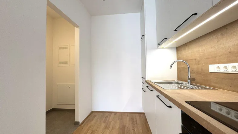 Moderne Küche mit weißen Schränken, Holzarbeitsplatte und Parkettboden in einem hellen Raum.