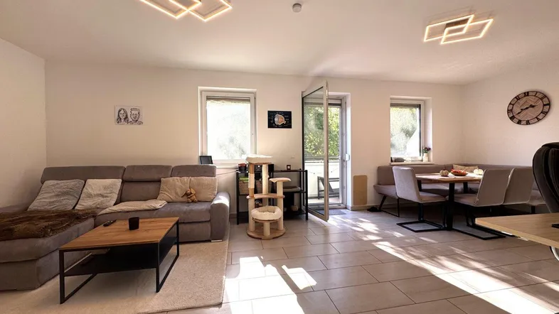 Heller, offener Wohn- und Essbereich mit modernen Deckenleuchten, Fliesenboden und Zugang zum Balkon.