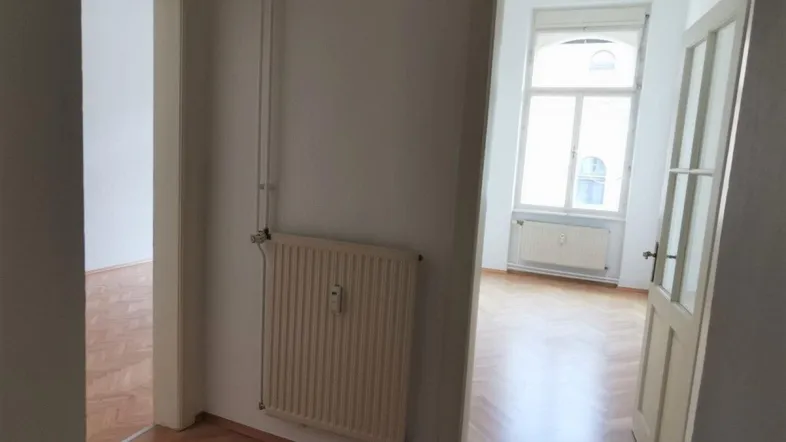 Flur mit Heizkörper und Blick in angrenzende Zimmer mit Parkettboden und Fenstern.