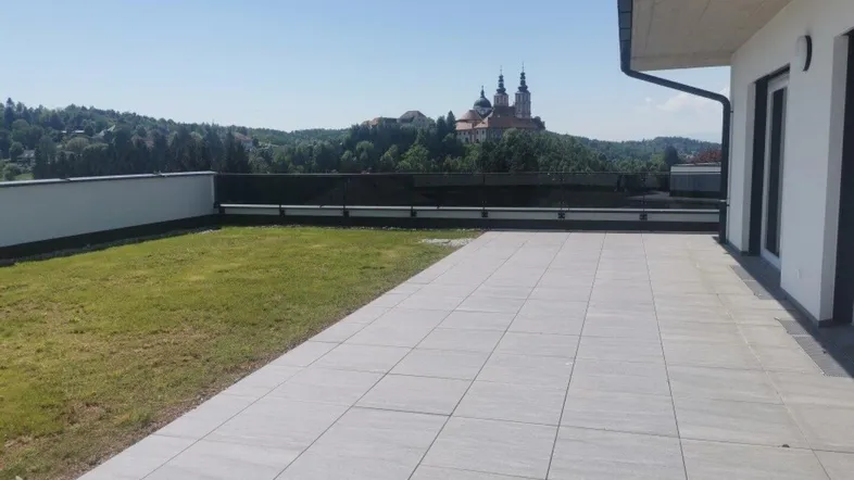 Große geflieste Terrasse mit Rasenfläche und weitem Blick auf ein historisches Gebäude.