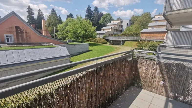 Balkon mit Holzsichtschutz und Blick auf die grüne Umgebung und weitere Gebäude.