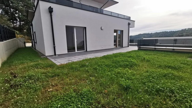 Modernes Gebäude mit weißer Fassade, Terrasse und Rasenfläche im Gartenbereich.