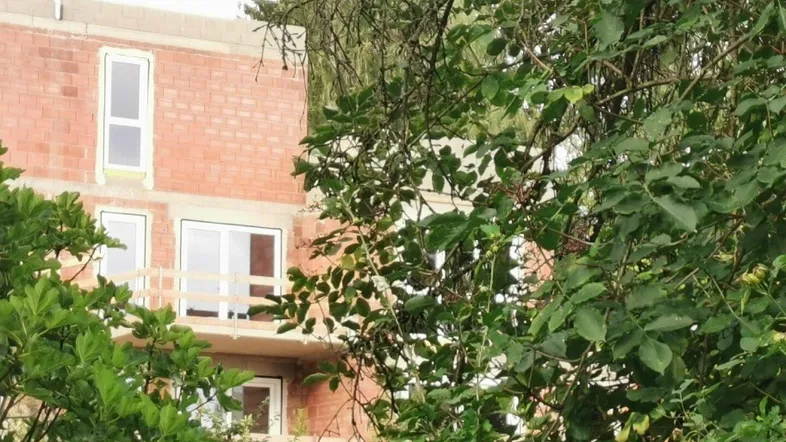 Neubauwohnung im Rohbau mit sichtbaren Ziegelwänden und Balkonen, umgeben von Bäumen.