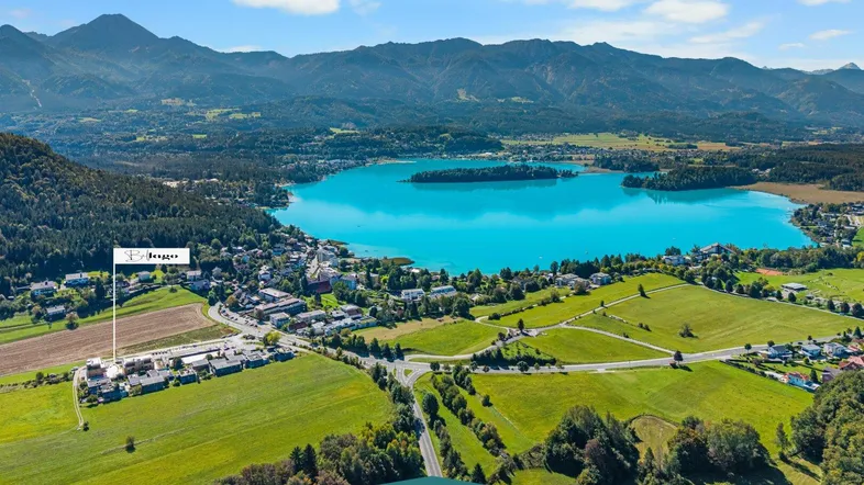 Panoramablick auf den Faaker See mit umliegender Landschaft und Bergen, inklusive Standortmarkierung.