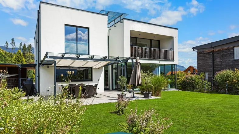Moderne Villa mit großer Rasenfläche, überdachter Terrasse und Bergblick.