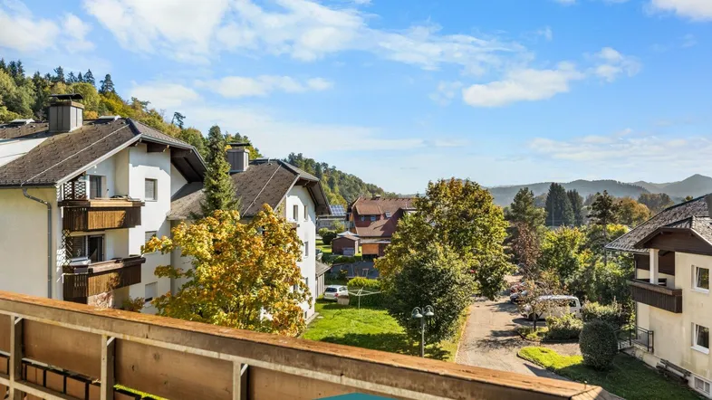 Blick vom Balkon auf die umliegende Wohngegend und die bewaldeten Hügel unter blauem Himmel.