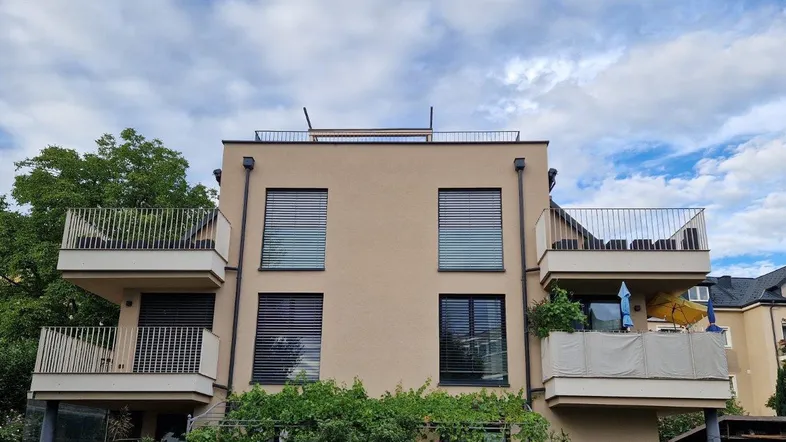 Modernes Mehrfamilienhaus mit mehreren Balkonen und beiger Fassade unter bewölktem Himmel.